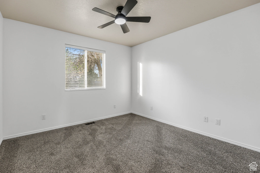 Spare room featuring a ceiling fan, dark colored carpet, and baseboards