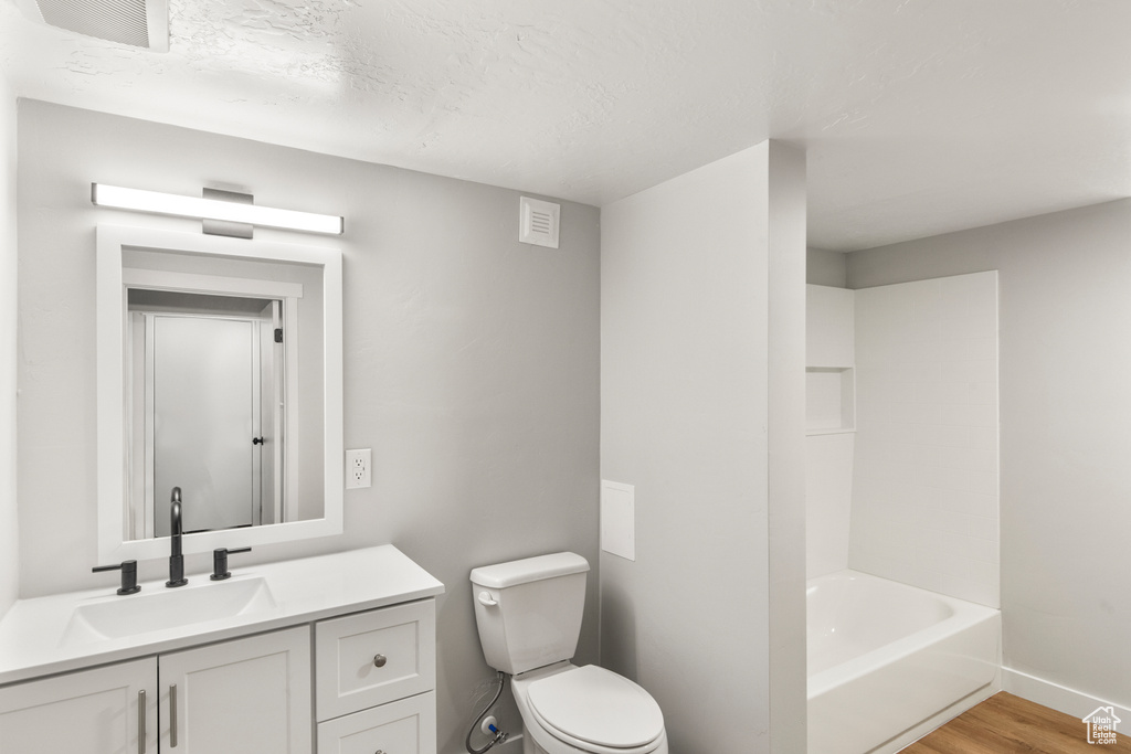 Bathroom with toilet, wood finished floors, baseboards, vanity, and a textured ceiling