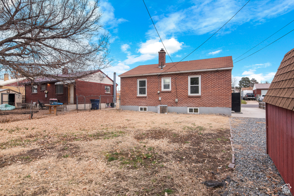 Rear view of house featuring a chimney, brick siding, fence, and a shingled roof