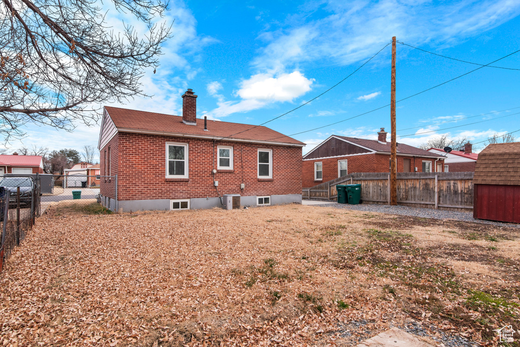Back of property featuring brick siding, a chimney, a fenced backyard, central AC unit, and a shingled roof
