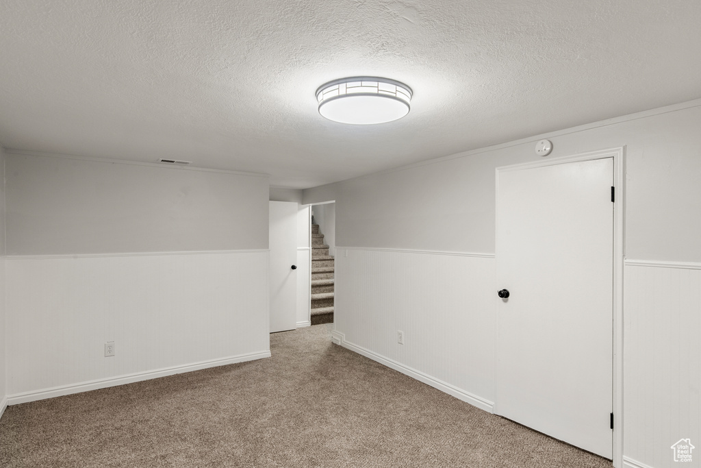 Empty room with a textured ceiling, stairway, and carpet flooring