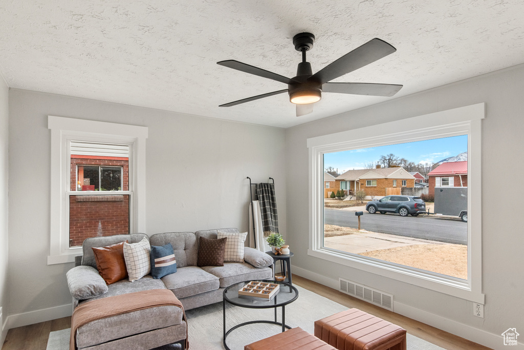 Living area with light wood-type flooring, baseboards, ceiling fan, and a textured ceiling