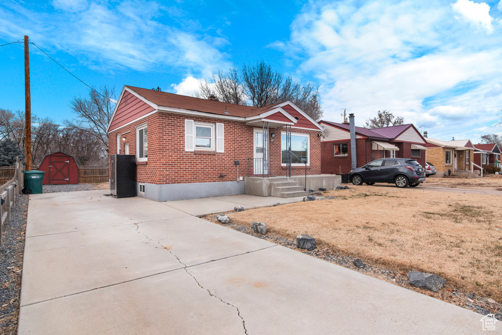 View of front of home with brick siding, a shed, concrete driveway, an outdoor structure, and fence