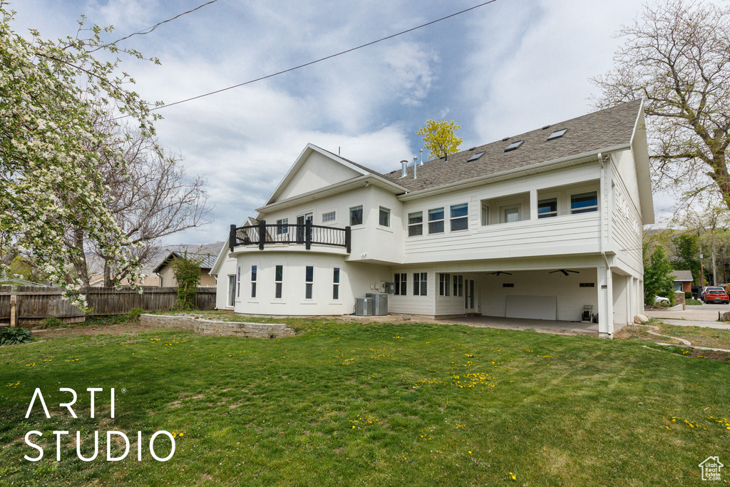 Rear view of house with a yard, fence, central AC unit, and a balcony