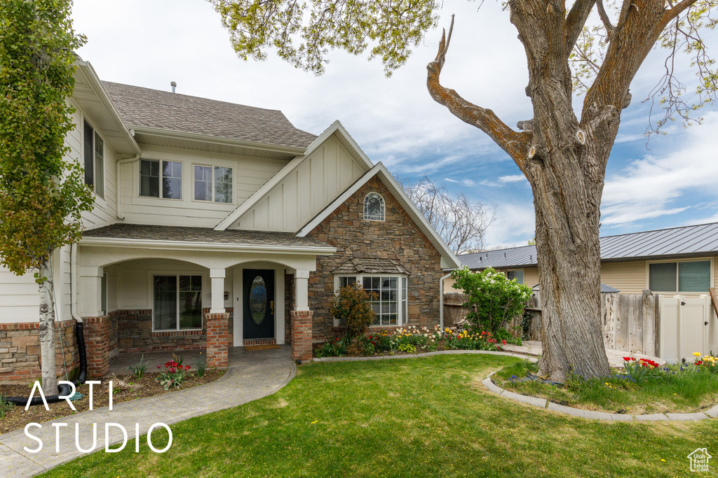 View of front of home featuring stone siding, board and batten siding, fence, and a front yard