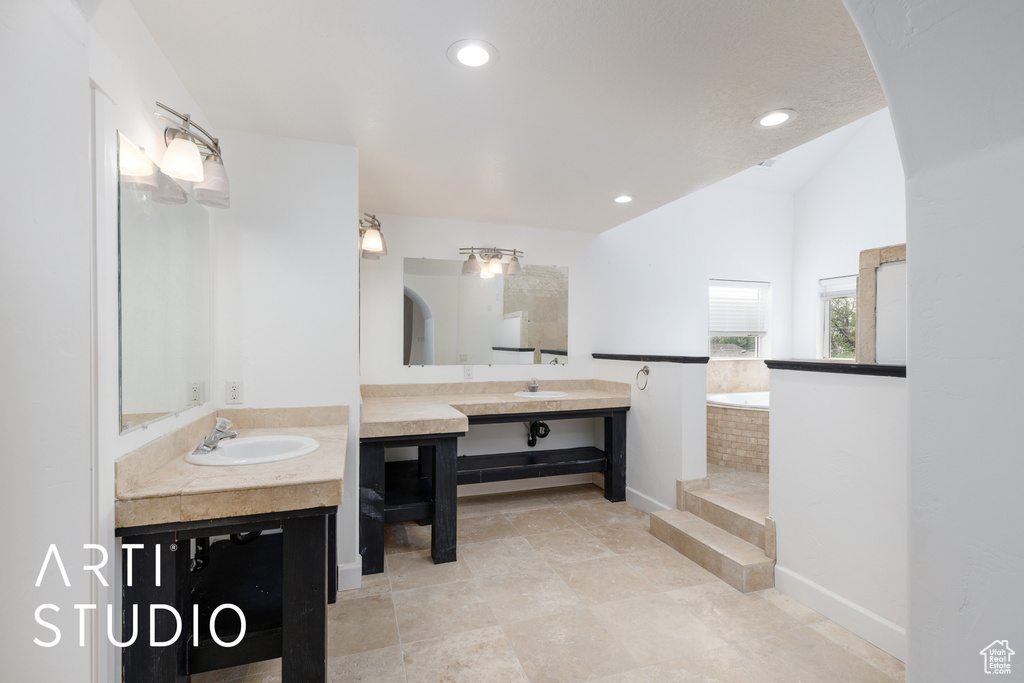 Full bathroom with a sink, two vanities, a bath, baseboards, and lofted ceiling