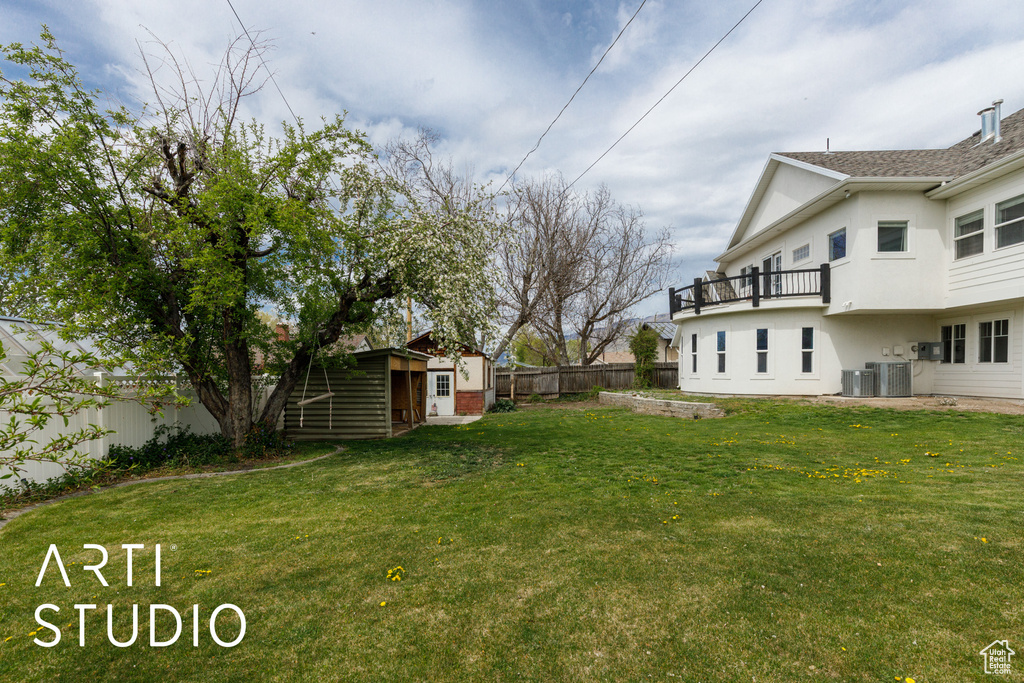 View of yard featuring central AC unit, fence, an outdoor structure, and a balcony