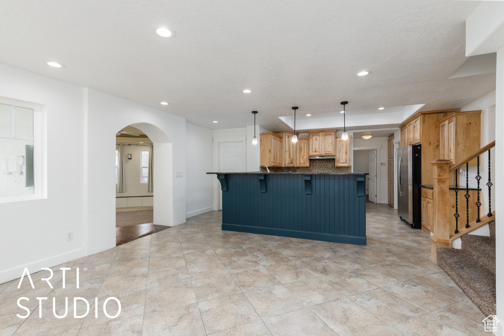 Kitchen with freestanding refrigerator, dark countertops, a kitchen breakfast bar, and recessed lighting