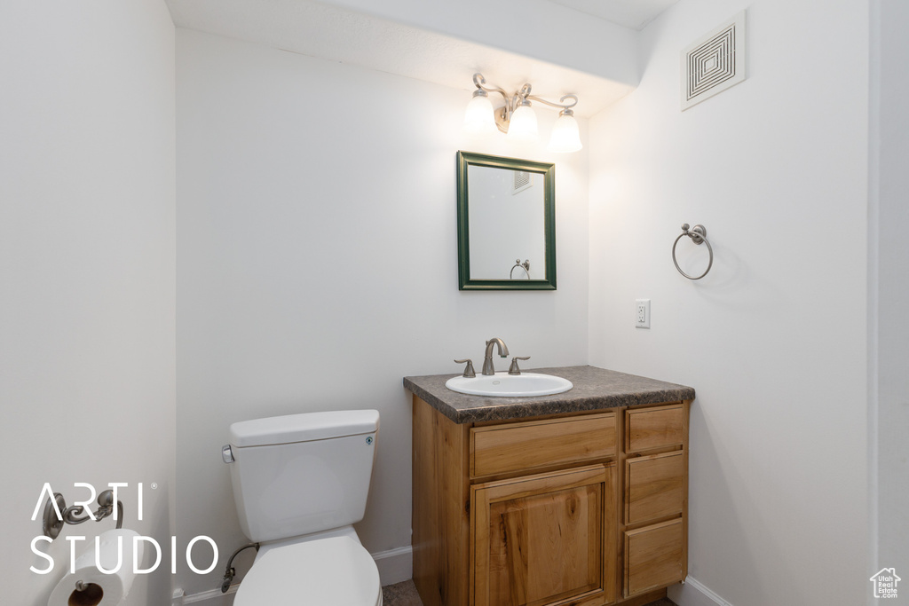 Half bath with vanity, toilet, baseboards, and visible vents