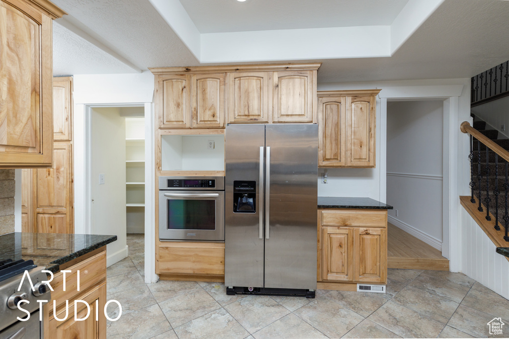 Kitchen featuring light brown cabinets, dark stone countertops, appliances with stainless steel finishes, and visible vents