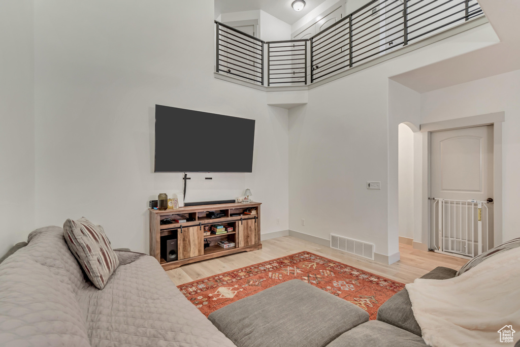 Living room with baseboards, visible vents, a towering ceiling, and wood finished floors