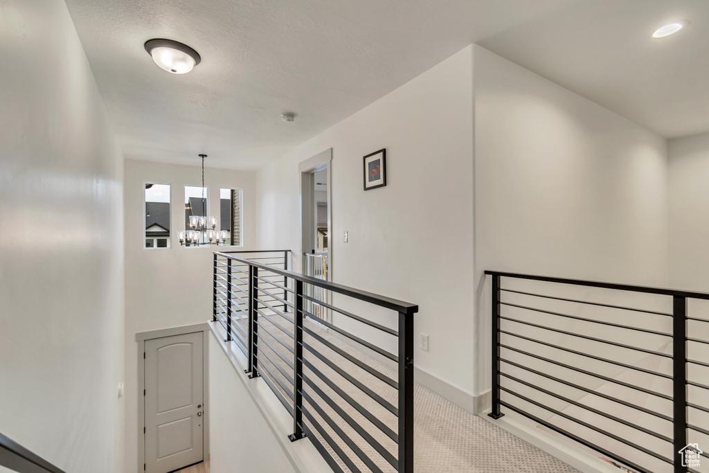 Hallway featuring a chandelier, carpet flooring, baseboards, and an upstairs landing