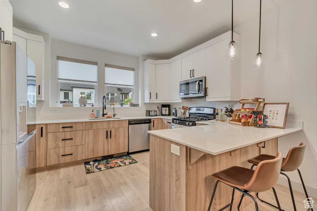 Kitchen with a sink, a peninsula, stainless steel appliances, recessed lighting, and light wood-style flooring
