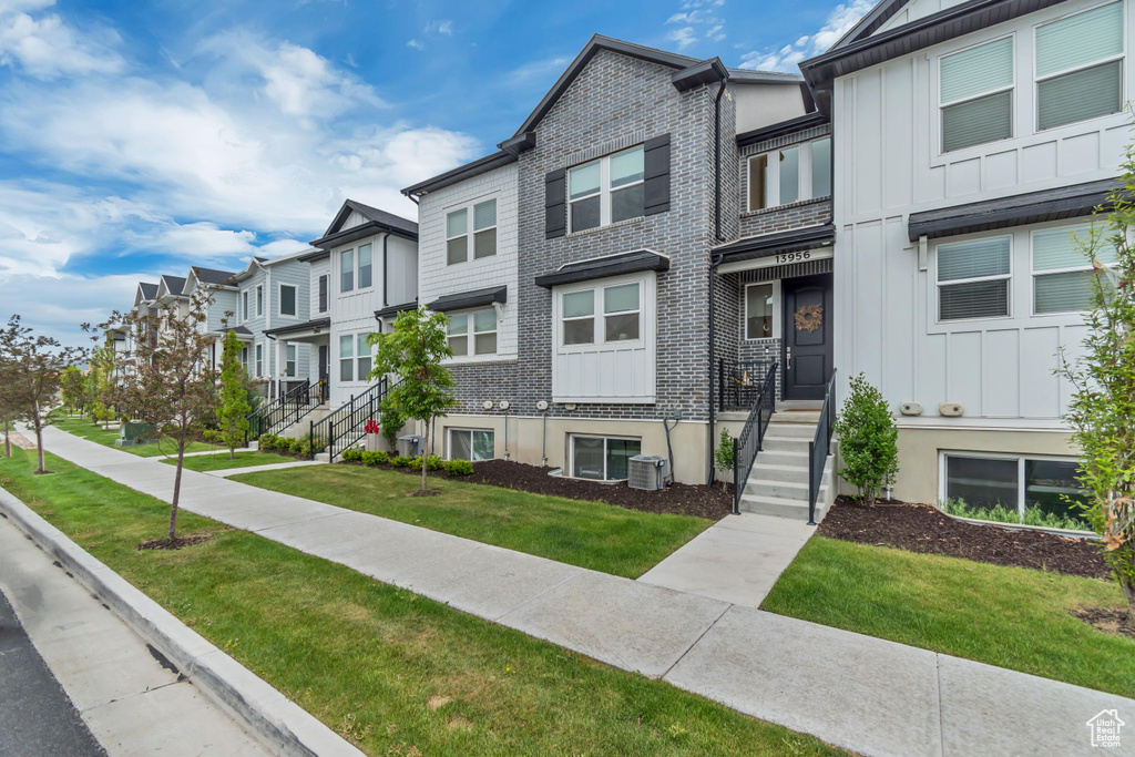 Townhome / multi-family property featuring central air condition unit, board and batten siding, a residential view, and a front lawn