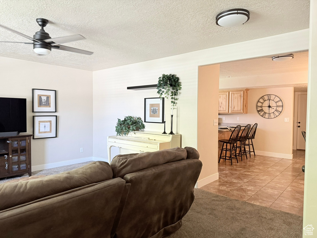 Living room with ceiling fan, light tile patterned floors, and a textured ceiling