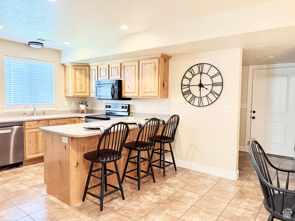 Kitchen with stainless steel appliances, light brown cabinetry, a textured ceiling, a kitchen breakfast bar, and a peninsula