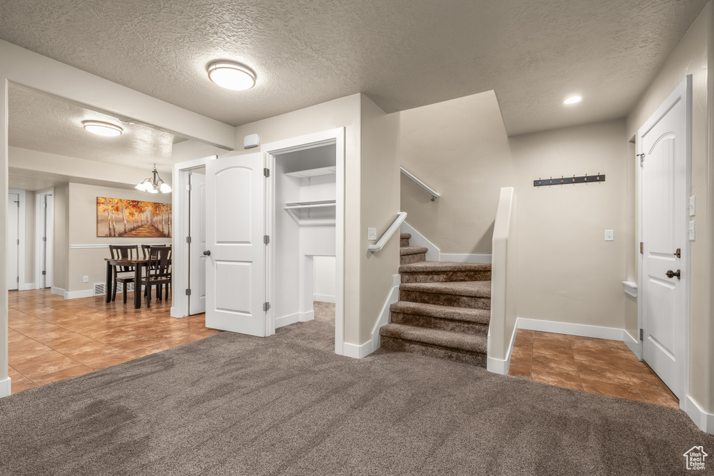 Carpeted entrance foyer featuring a textured ceiling, baseboards, a chandelier, stairs, and recessed lighting