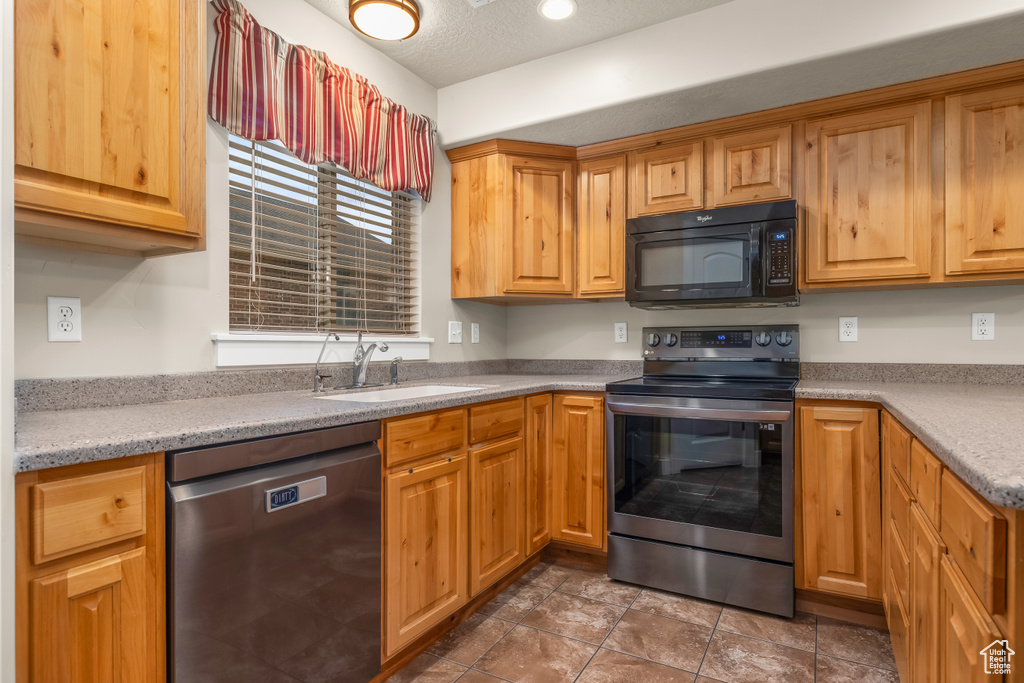 Kitchen featuring appliances with stainless steel finishes, a sink, light countertops, and stone finish flooring