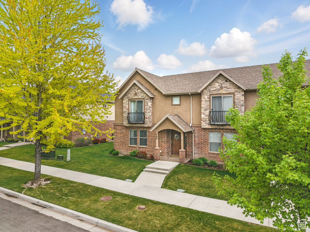 View of front facade featuring a front yard, stucco siding, stone siding, and a shingled roof