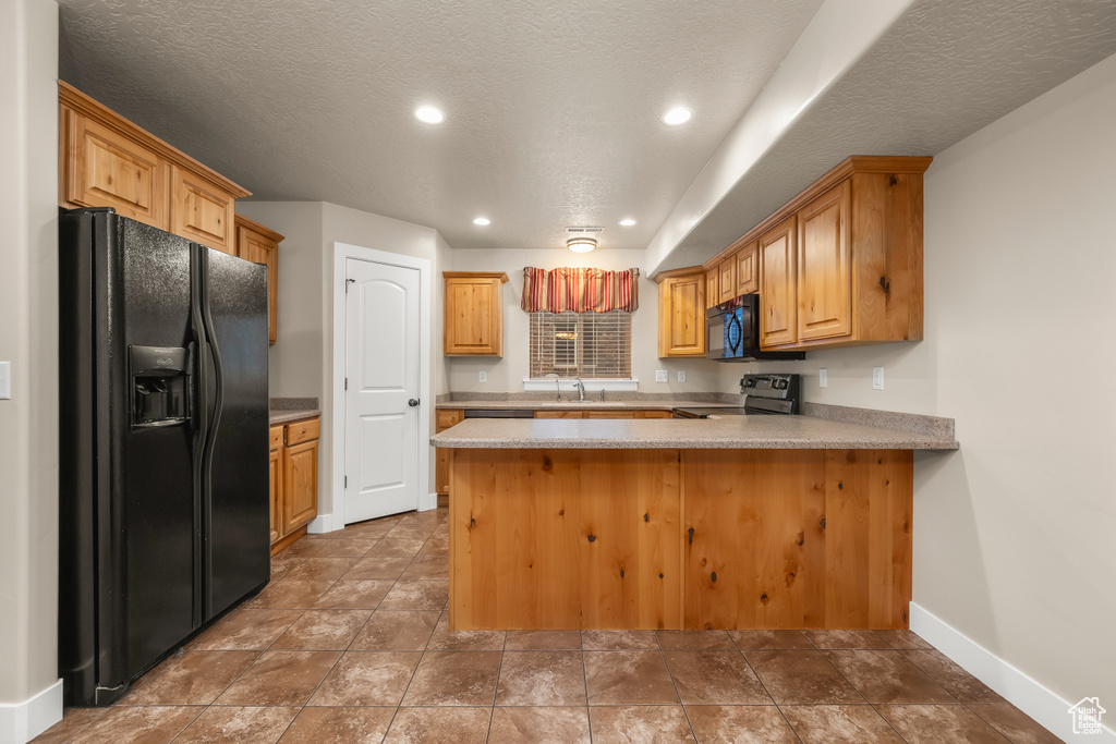 Kitchen featuring black appliances, a peninsula, baseboards, light countertops, and a sink