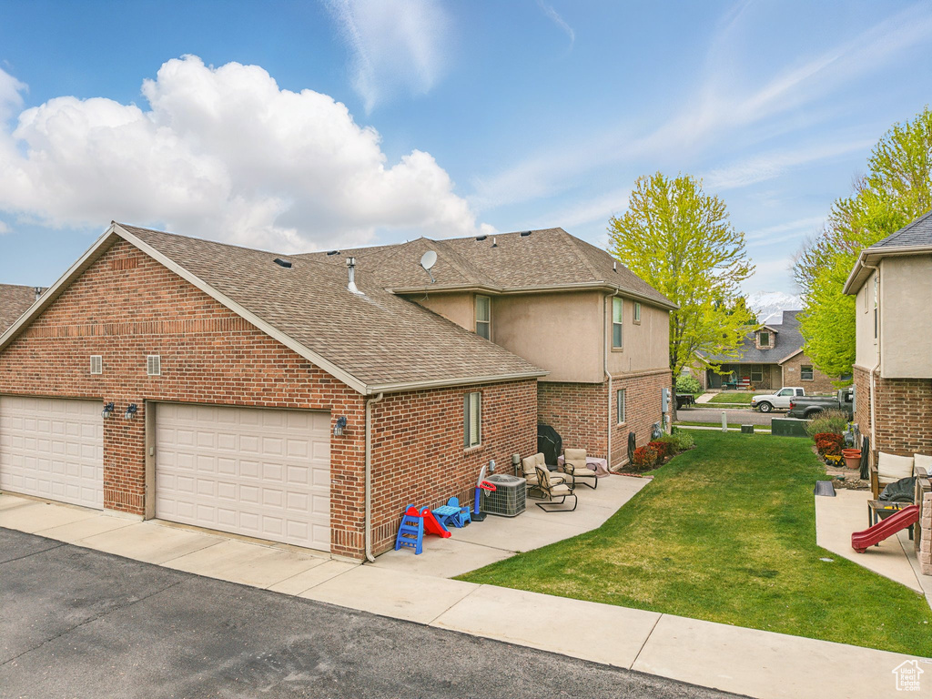 View of property exterior featuring roof with shingles, brick siding, cooling unit, a yard, and a patio area