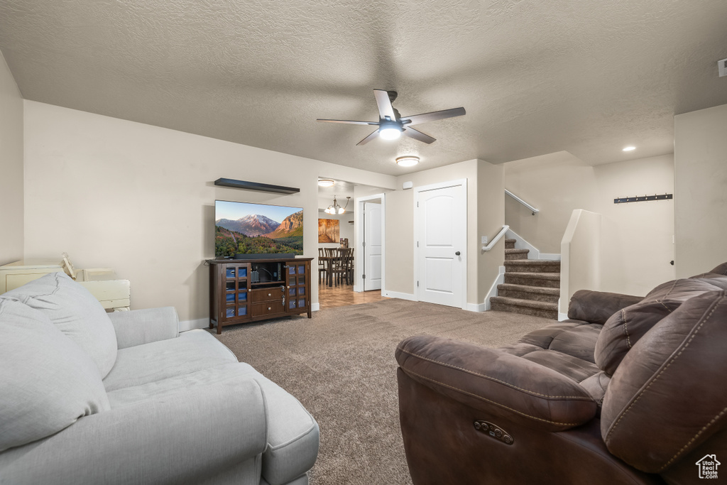 Living area featuring carpet, ceiling fan, stairs, baseboards, and a textured ceiling
