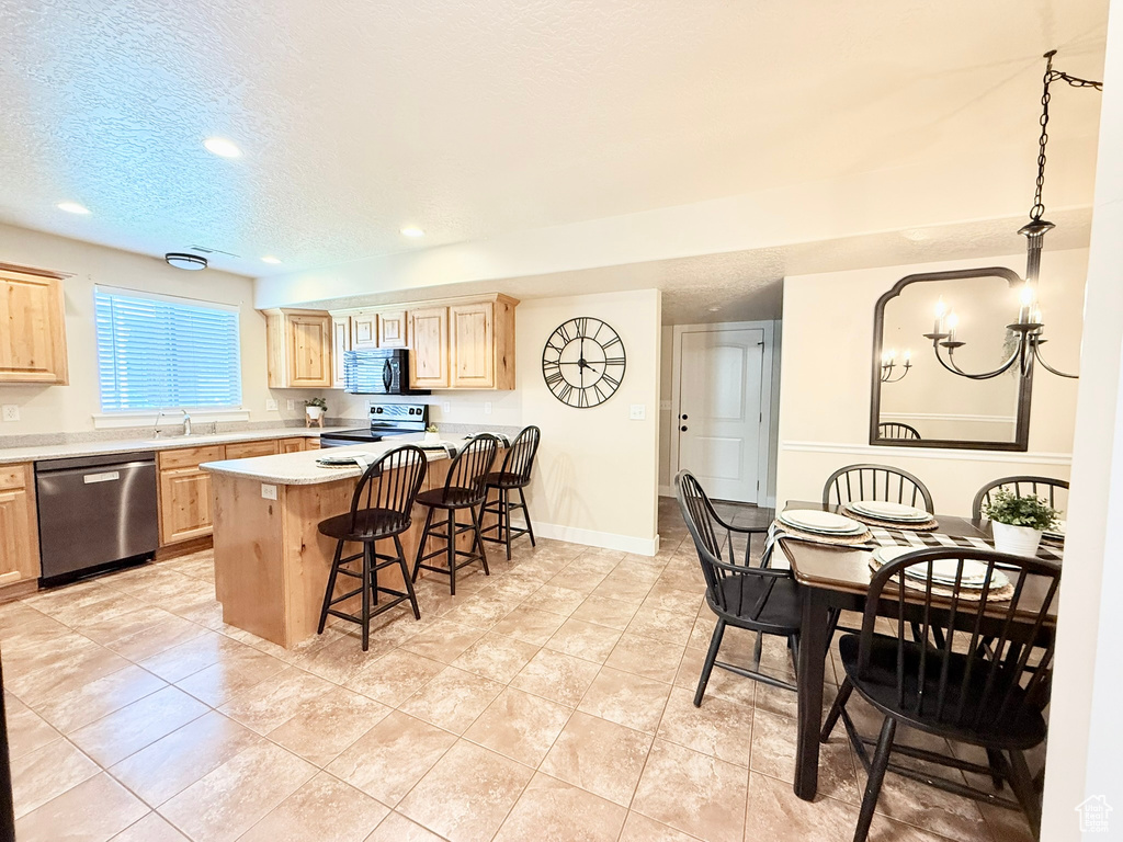 Kitchen featuring stainless steel appliances, light brown cabinets, a kitchen breakfast bar, light countertops, and recessed lighting