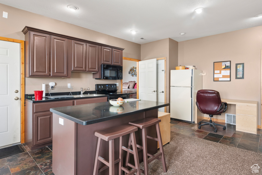 Kitchen featuring black appliances, stone tile flooring, dark countertops, a kitchen breakfast bar, and a kitchen island