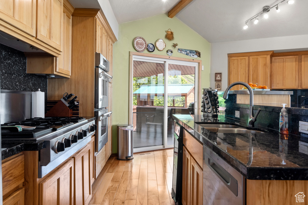 Kitchen featuring a sink, appliances with stainless steel finishes, light wood finished floors, tasteful backsplash, and dark stone countertops