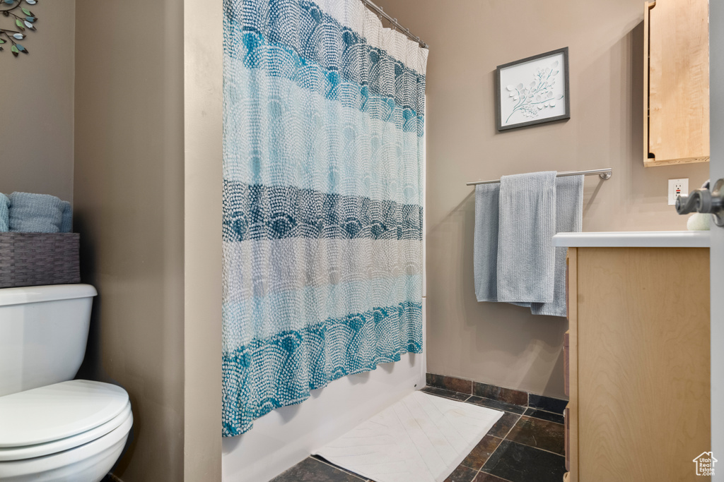 Full bath with toilet, baseboards, stone tile flooring, vanity, and shower / tub combo with curtain