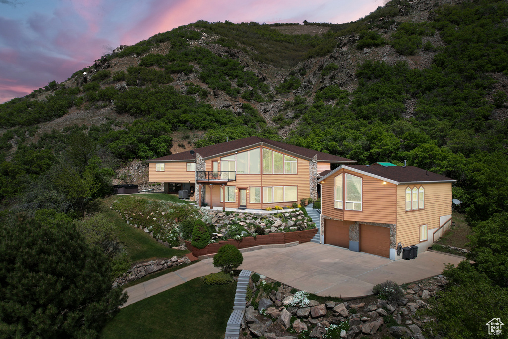 Back of house at dusk with an attached garage, concrete driveway, and a mountain view