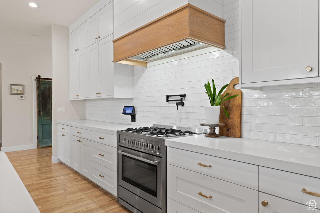 Kitchen featuring light countertops, white cabinetry, stainless steel range, and custom exhaust hood
