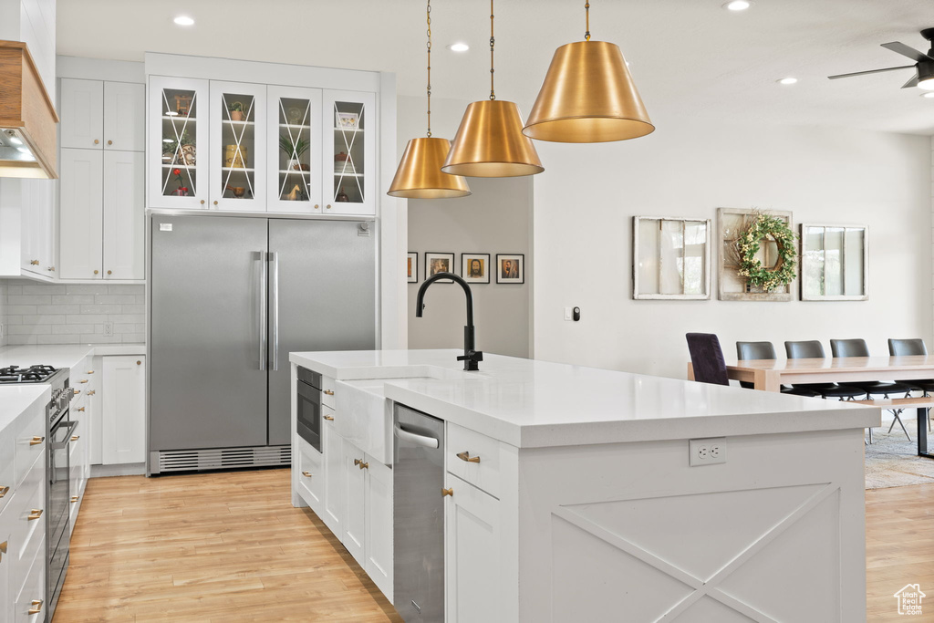 Kitchen with built in appliances, recessed lighting, a kitchen island with sink, and light wood-type flooring