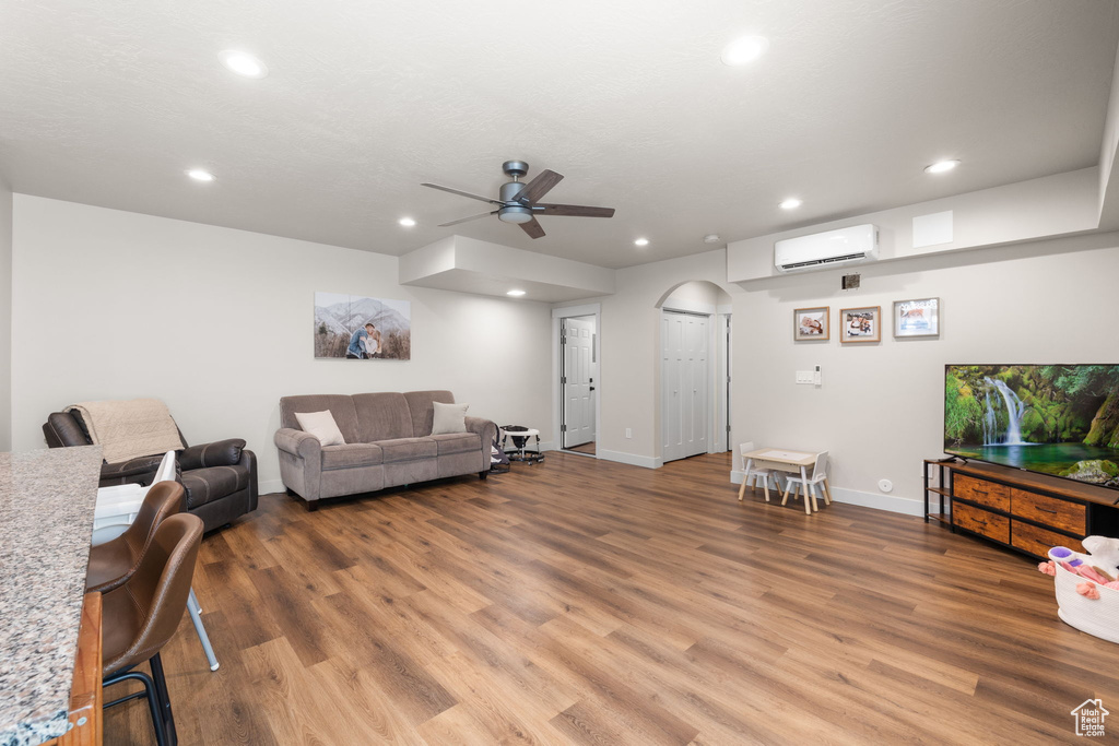 Living area featuring arched walkways, a ceiling fan, a wall mounted AC, and light wood-style flooring