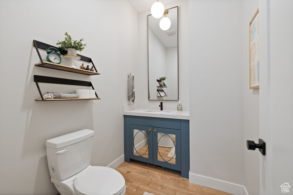 Half bathroom featuring visible vents, wood finished floors, vanity, baseboards, and toilet