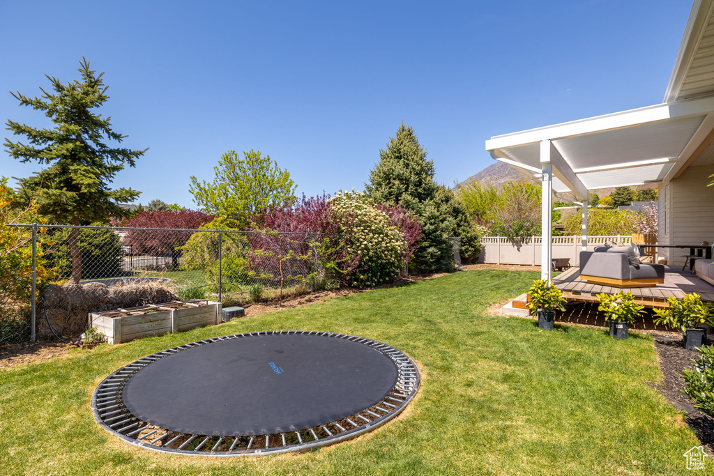 View of yard featuring a fenced backyard, a wooden deck, and a trampoline