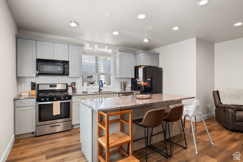 Kitchen with a sink, decorative backsplash, a breakfast bar area, and black appliances