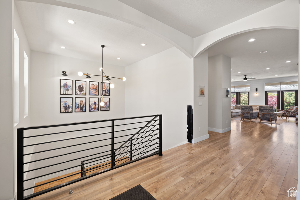 Corridor with an inviting chandelier, wood finished floors, recessed lighting, arched walkways, and an upstairs landing