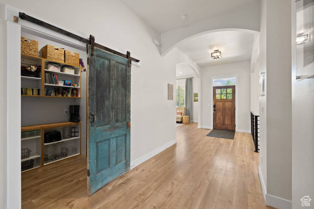 Foyer entrance with a barn door, arched walkways, baseboards, and wood finished floors