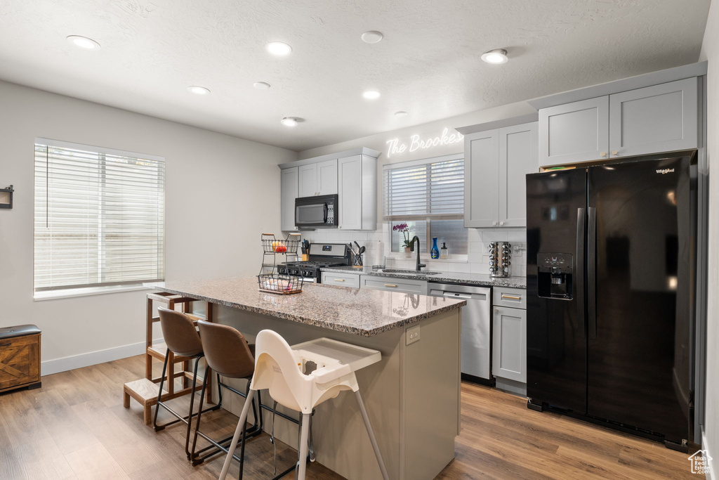 Kitchen featuring a kitchen island, a kitchen breakfast bar, tasteful backsplash, a sink, and black appliances