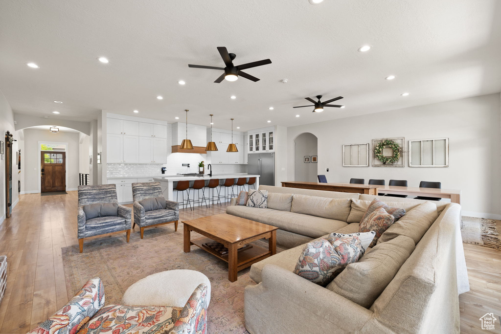 Living room featuring arched walkways, a ceiling fan, recessed lighting, baseboards, and light wood-type flooring