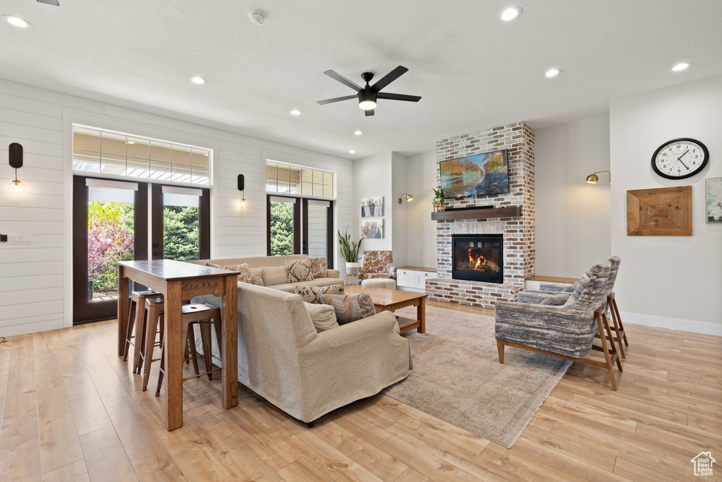 Living area featuring a brick fireplace, light wood-style floors, baseboards, ceiling fan, and recessed lighting
