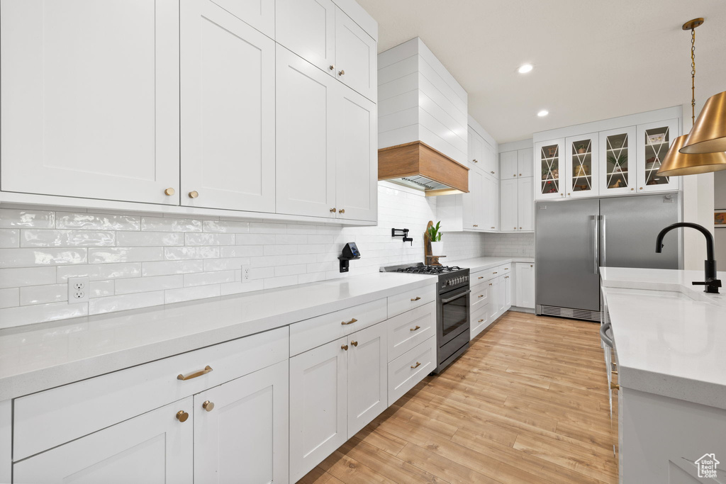 Kitchen featuring custom exhaust hood, light countertops, white cabinets, tasteful backsplash, and premium appliances