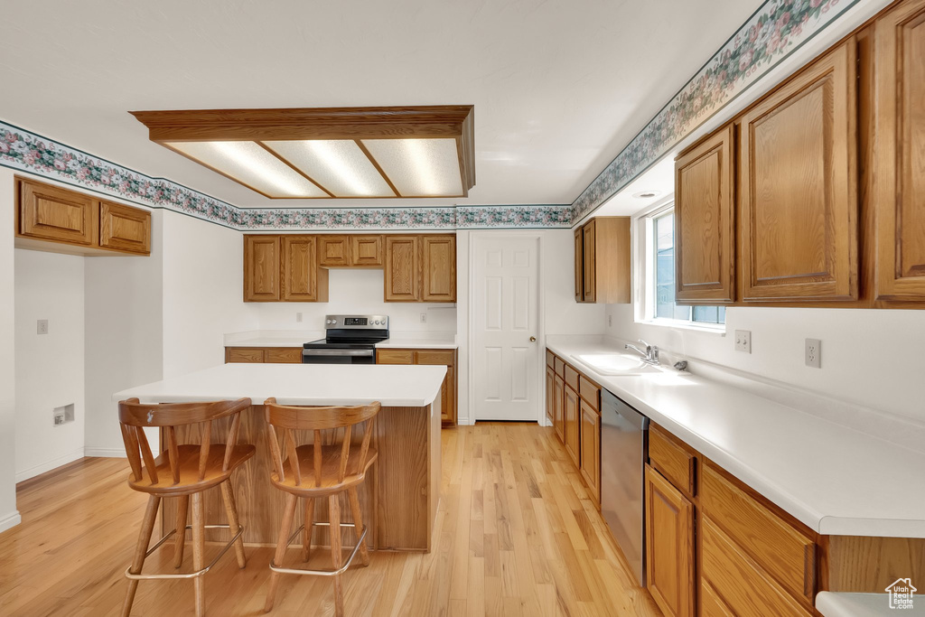 Kitchen featuring appliances with stainless steel finishes, light wood-style floors, brown cabinets, and light countertops