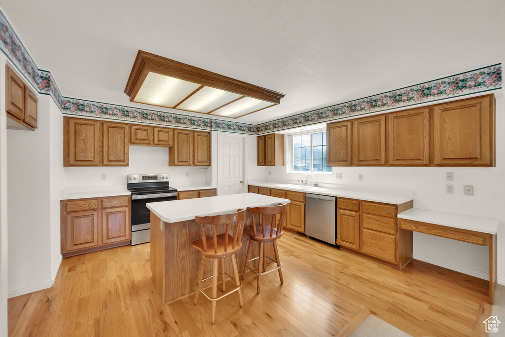 Kitchen featuring appliances with stainless steel finishes, a sink, light wood finished floors, and a breakfast bar