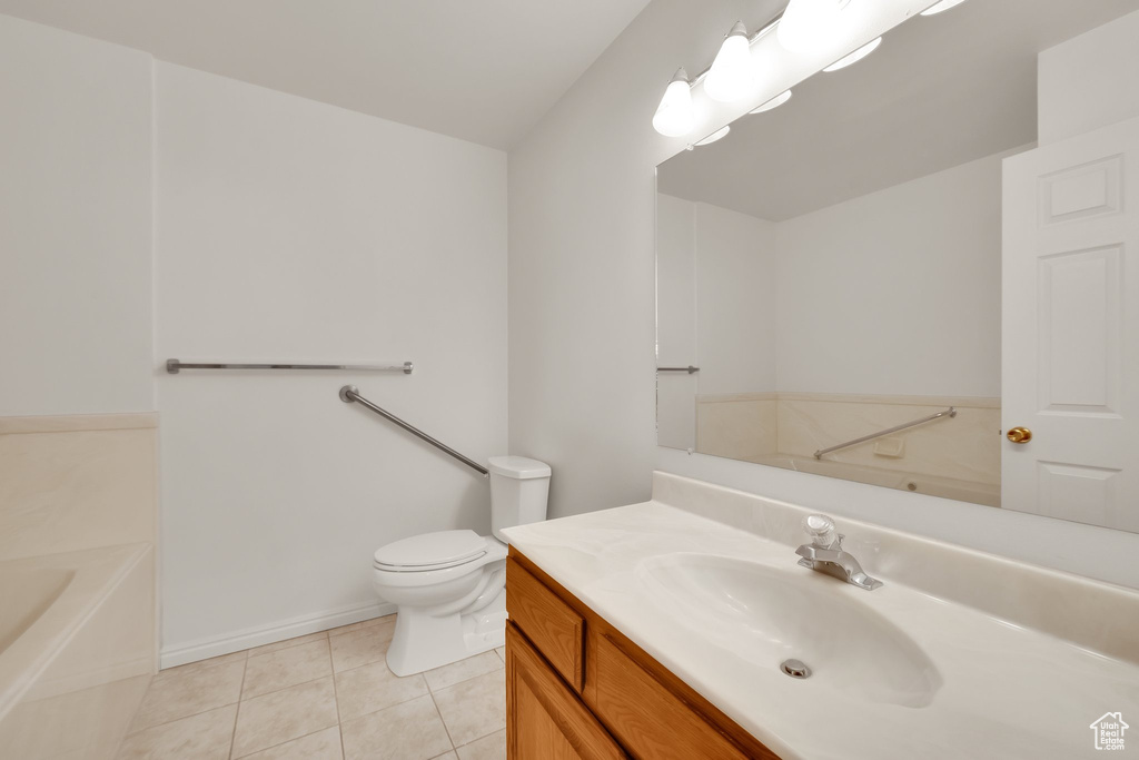 Bathroom featuring tile patterned flooring, vanity, toilet, a bath, and baseboards