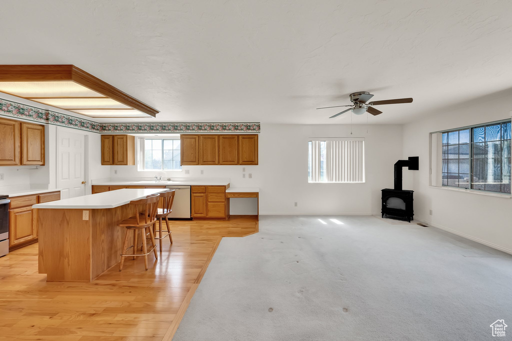 Kitchen featuring appliances with stainless steel finishes, a wood stove, a ceiling fan, a breakfast bar, and light countertops