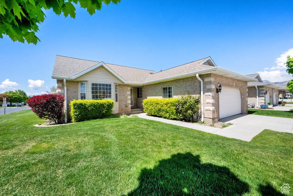 Ranch-style home featuring a garage, a front lawn, concrete driveway, and roof with shingles