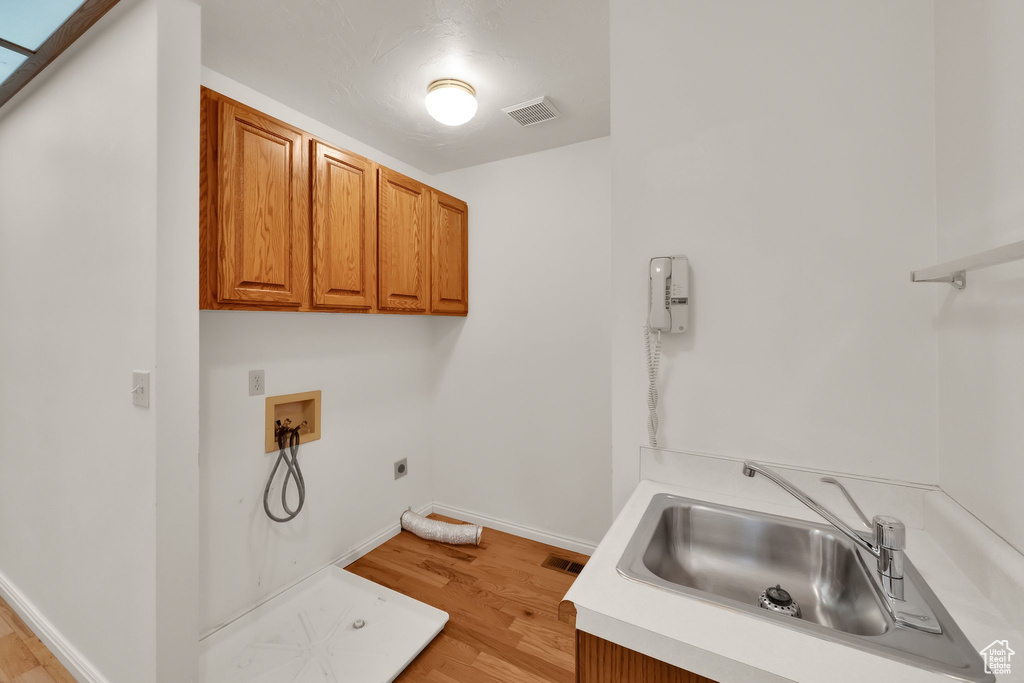 Laundry area with electric dryer hookup, cabinet space, washer hookup, and light wood-style flooring