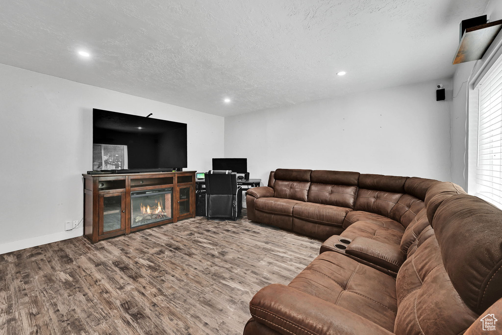 Living area with wood finished floors, recessed lighting, a textured ceiling, a glass covered fireplace, and baseboards